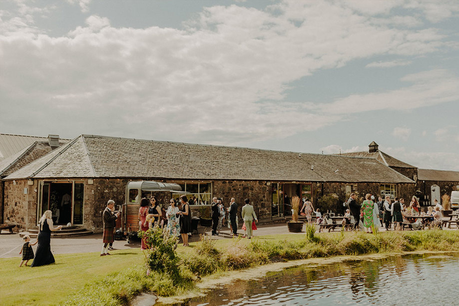 Wedding guests outside a barn on a sunny day