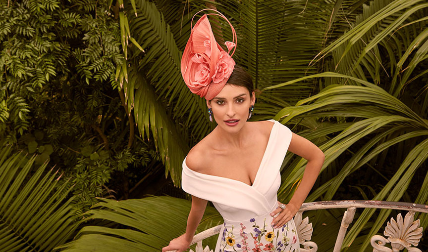 a person in a floral Veni Infantino dress and hat posing for a picture against leafy green plants