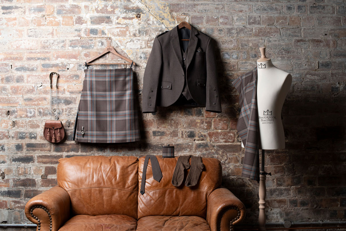 a brown leather sofa with a Jura Mist tartan kilt, a jacket and a sporran hanging above it.