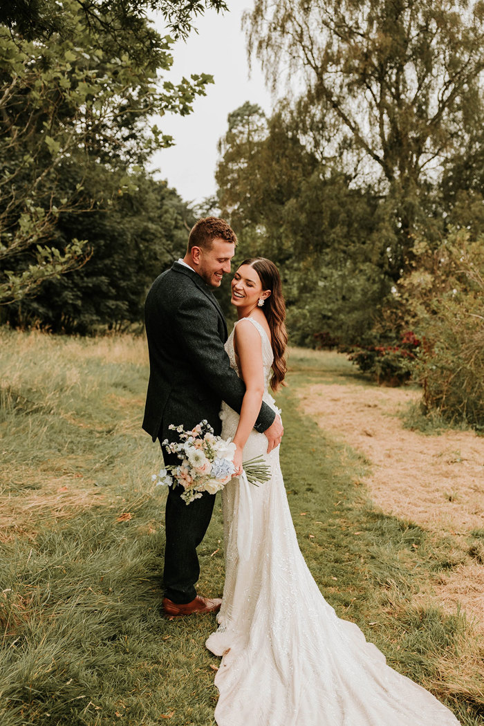 a smiling bride and groom Matt Fagerson standing on grass in the grounds of Dunglass Estate