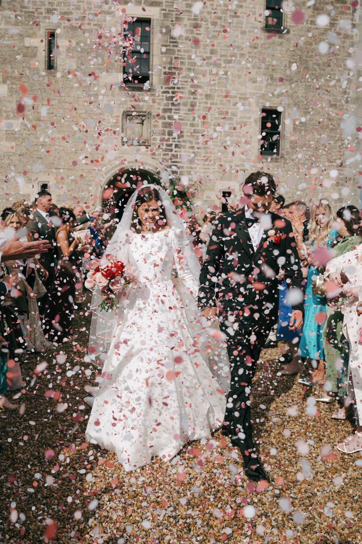 Newlyweds Nicole and Ryan walk through a shower of pink-and-white confetti outside Barnbougle Castle as their wedding guests celebrate.
