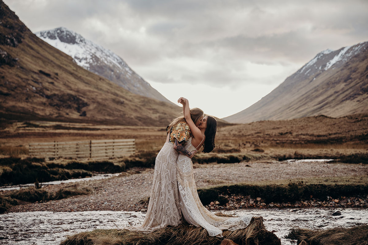 Couple sharing a kiss beside a river during a dramatic Glencoe elopement shoot in the Scottish Highlands.