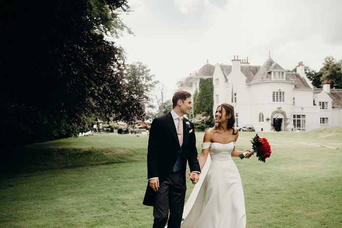 a bride and groom walking in a garden in front of the white exterior of Achnagairn Castle