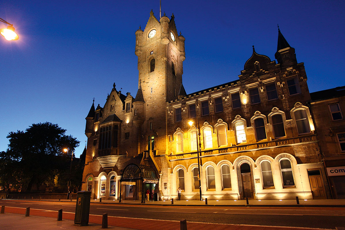 exterior of large town hall building, complete with clocktower, lit up in the evening by yellow glow of streetlights