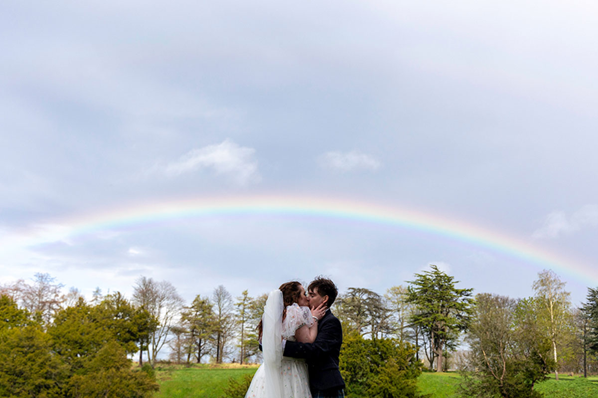 A couple kiss underneath a rainbow