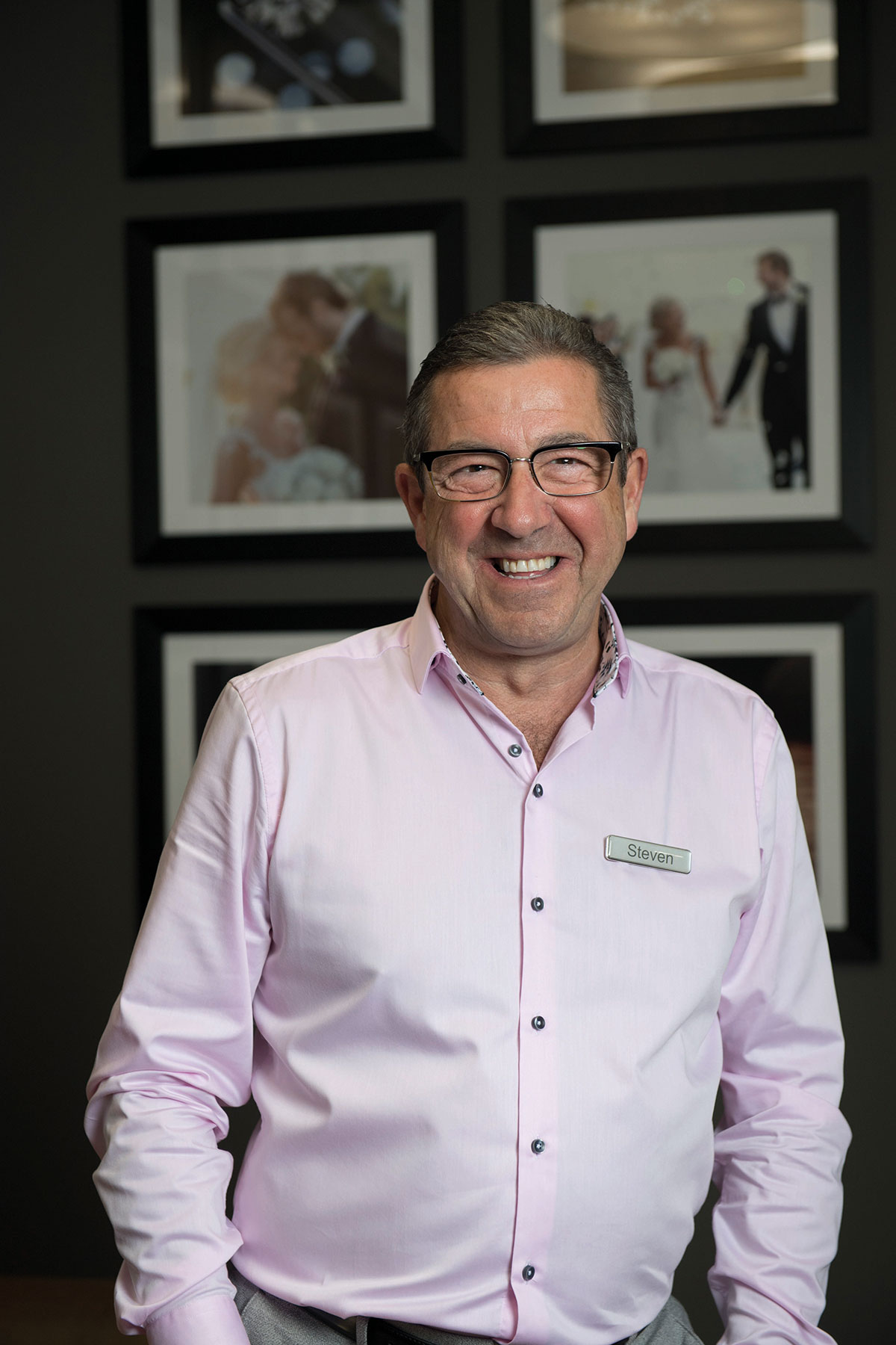 a grey haired man, wearing glasses and smiling in a pink button-up shirt and a name tag that says 'Steven' 