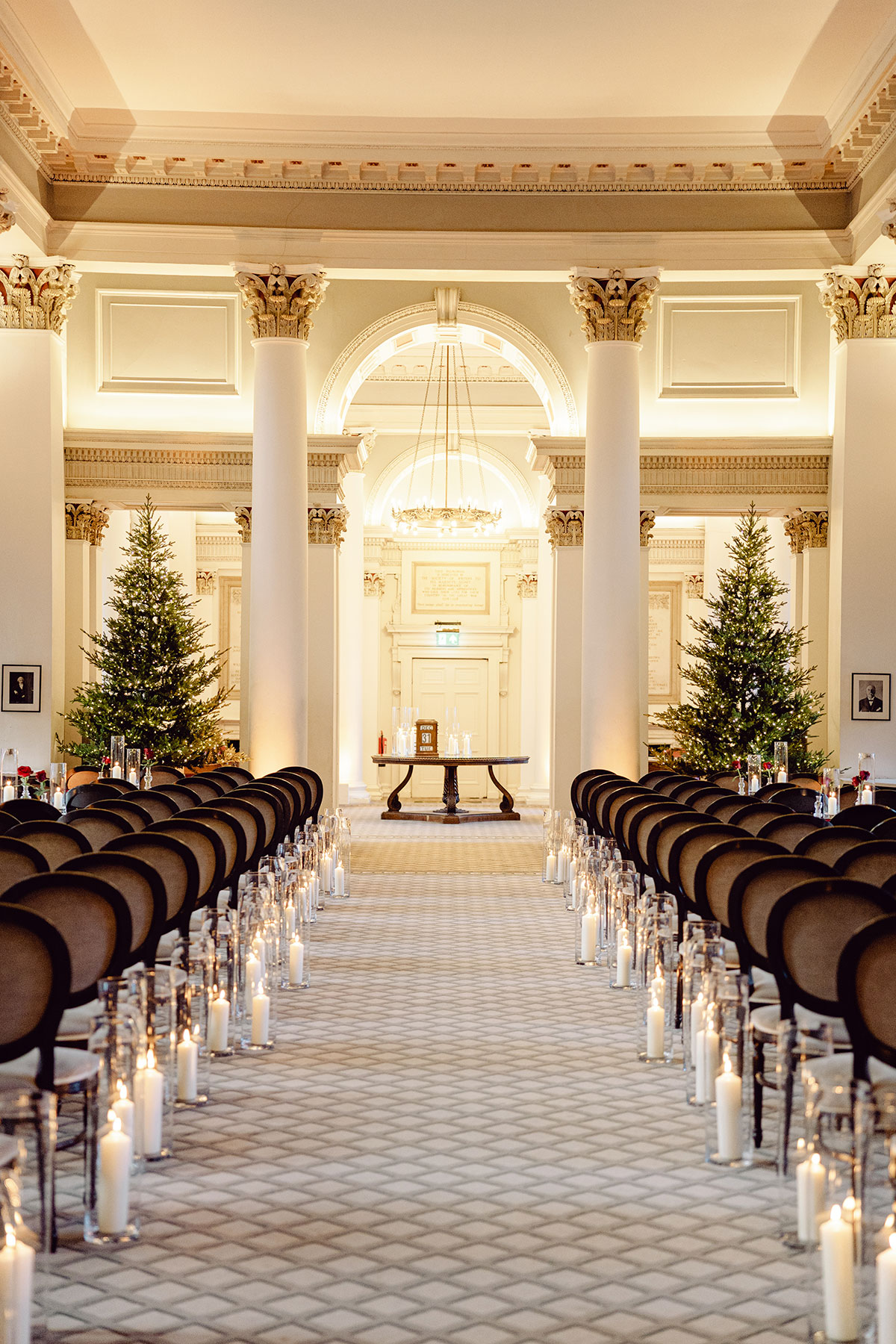 Ceremony setup at The Signet Library in Edinburgh, featuring rows of chairs, tall columns, candles lining the aisle and decorated Christmas trees