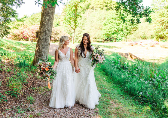 Two Brides Walking Hand In Hand In A Garden