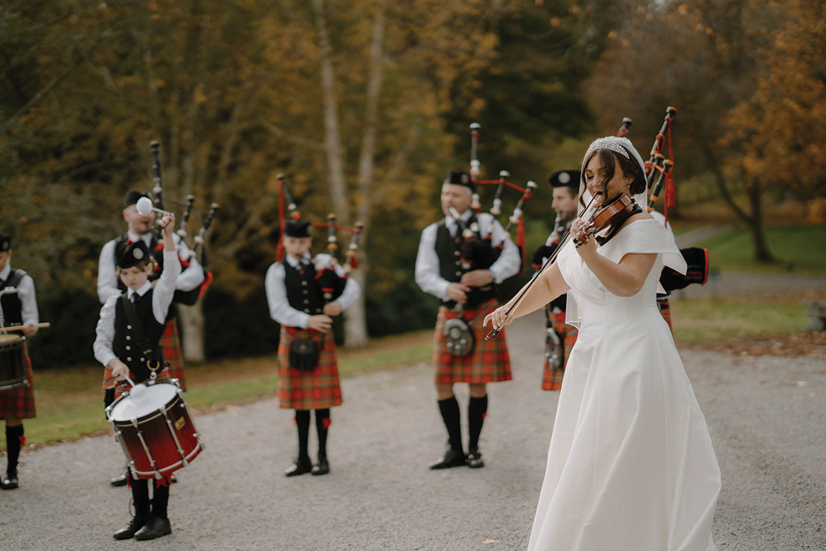 Bride performing on the violin alongside a pipe band at her Cluny Castle wedding in Aberdeenshire.