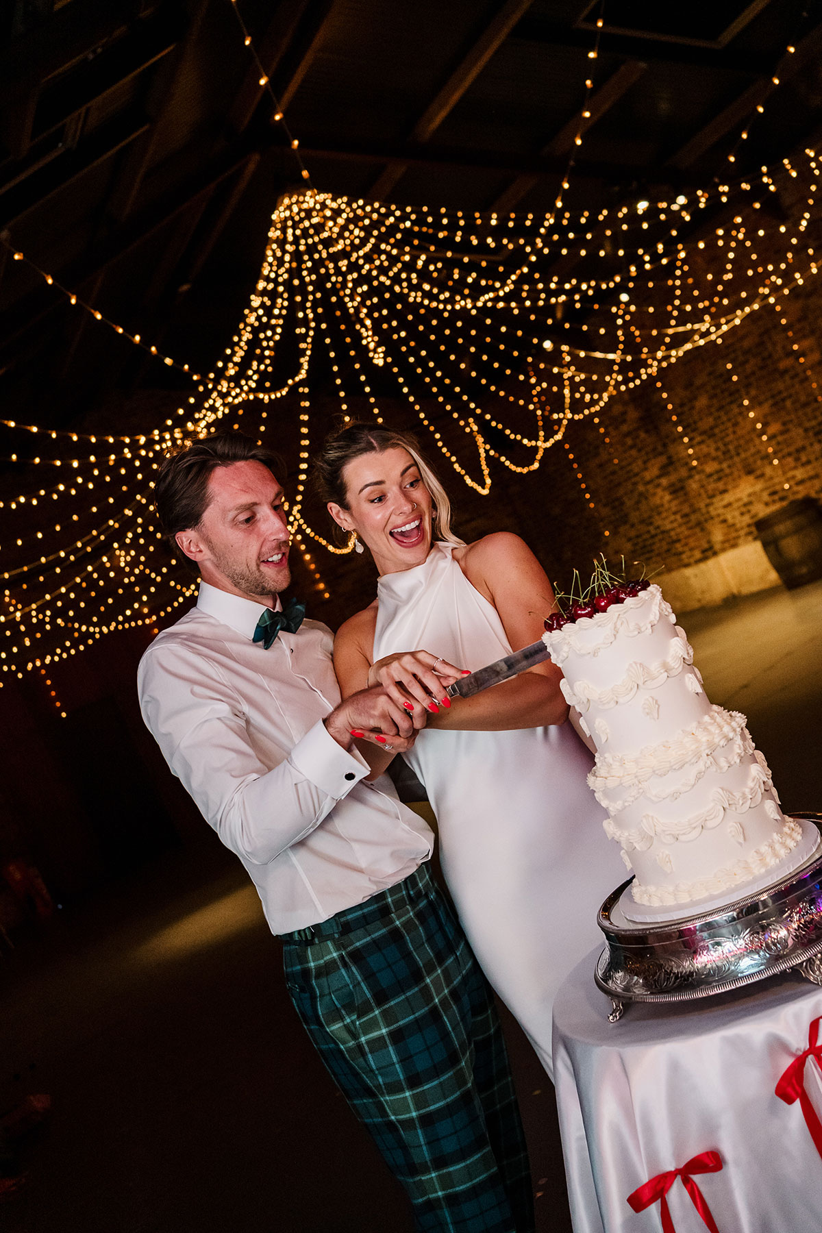 Bride and groom cutting cherry-topped wedding cake at Kinkell Byre in Fife.