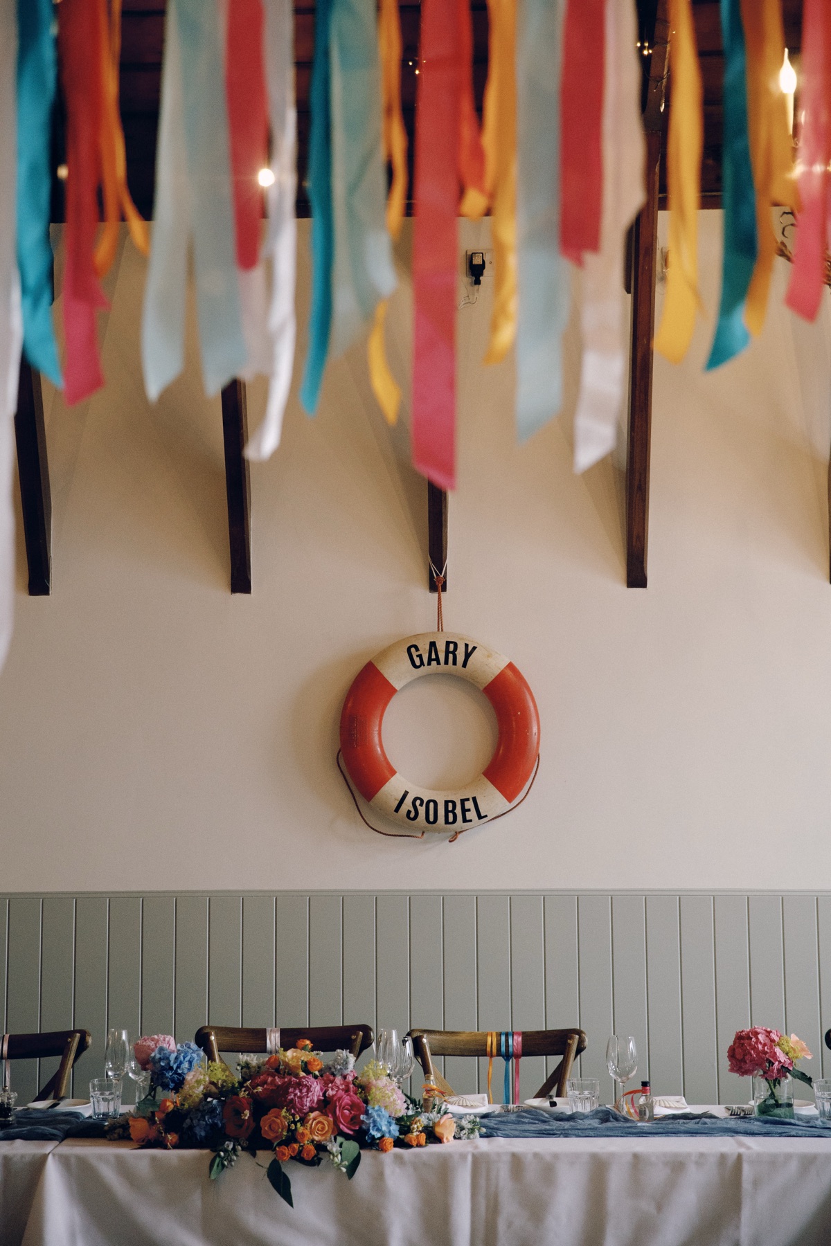 Personalised Gary and Isobel lifebuoy above colourful wedding flowers and ribbon decorations at The Dougarie Boathouse.