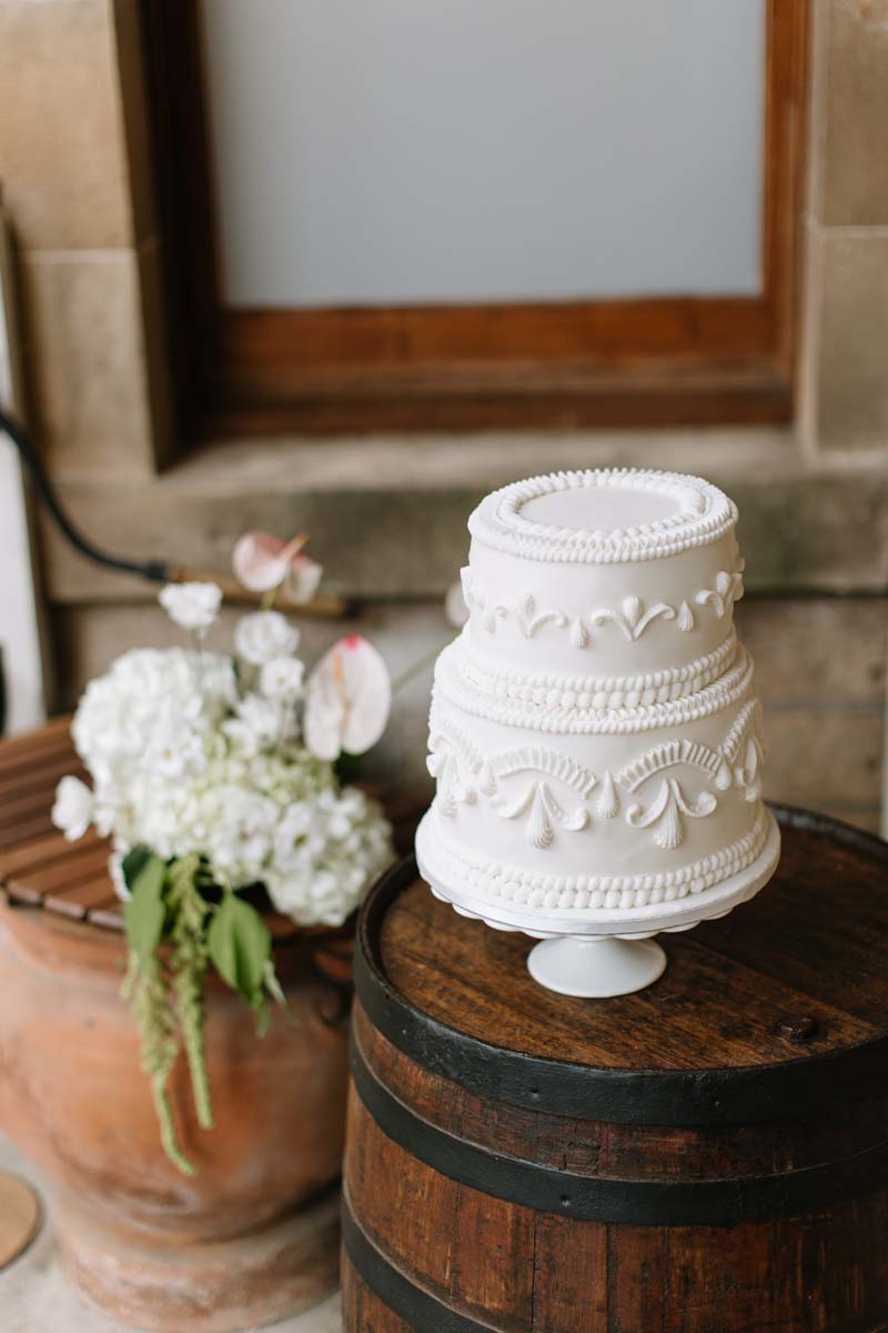 White two-tier wedding cake with Lambeth-style piping displayed on a wooden barrel at Cambo House in Fife.