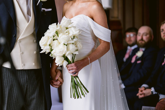 A person in a suit and a person in a white dress holding a bouquet of white roses.