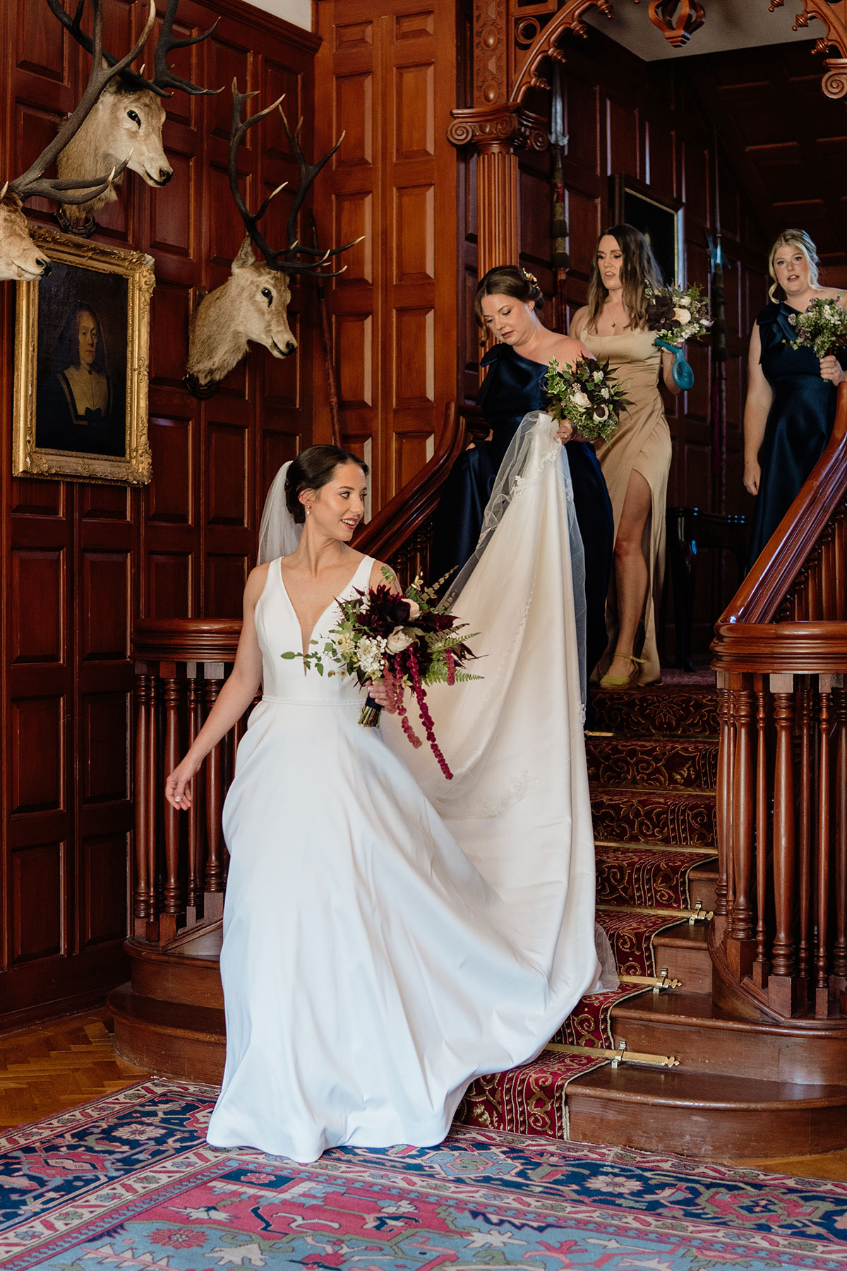 Bride walking down the grand staircase at Mar Lodge Estate with her bridesmaids before the wedding ceremony