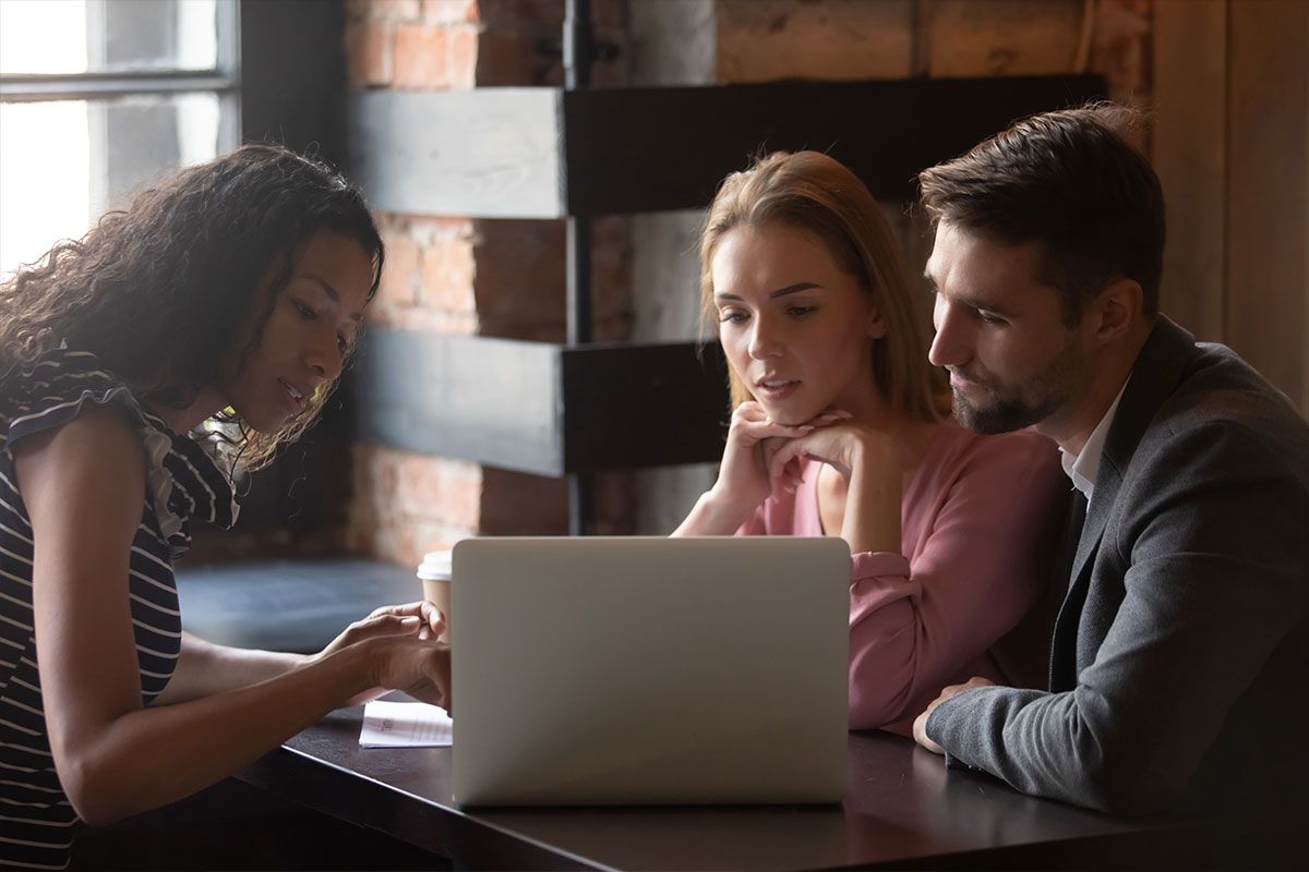 two women and one man looking at a laptop screen