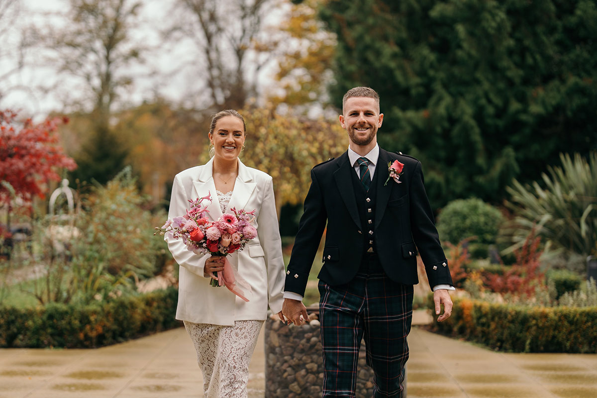 Bride and groom walk towards camera through Scottish wedding venue gardens in autumn