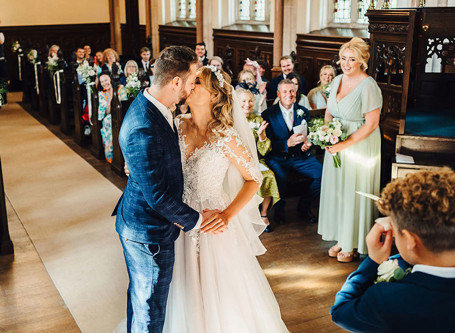 Bride and groom share their first kiss holding hands while everyone claps and smiles