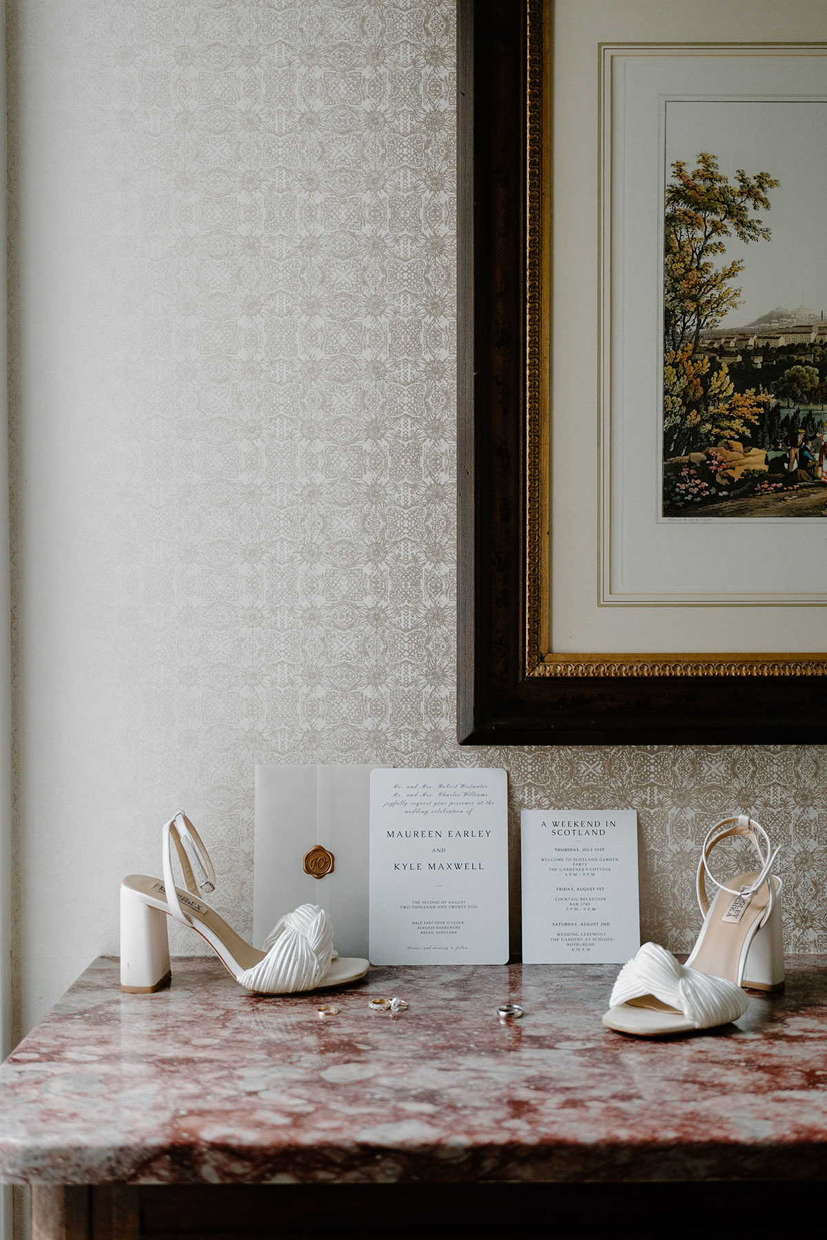 Wedding flat lay featuring white bridal heels, wedding invitations and rings styled on a pink marble table inside a Scottish wedding venue