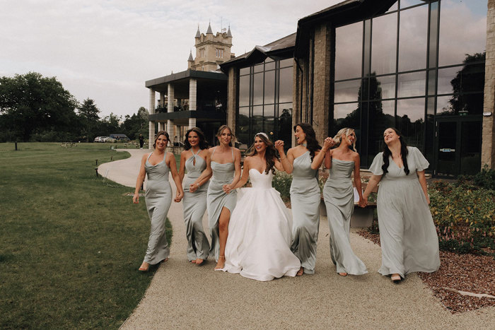 a bride and row of bridesmaids in pale green dresses walking hand-in-hand outside Cameron House.