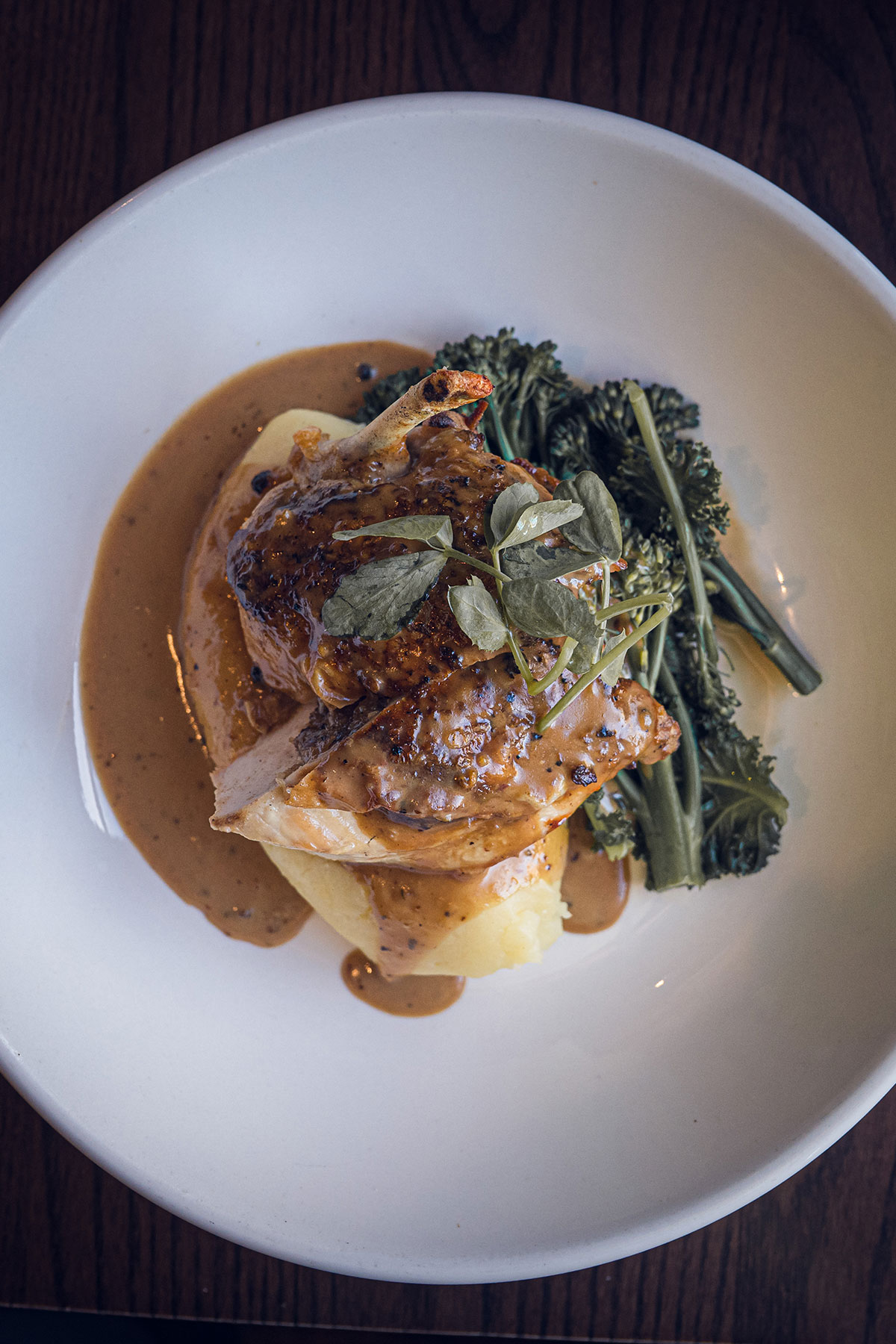 A plated chicken dish with mashed potatoes, broccolini and peppercorn sauce, served as part of a wedding menu