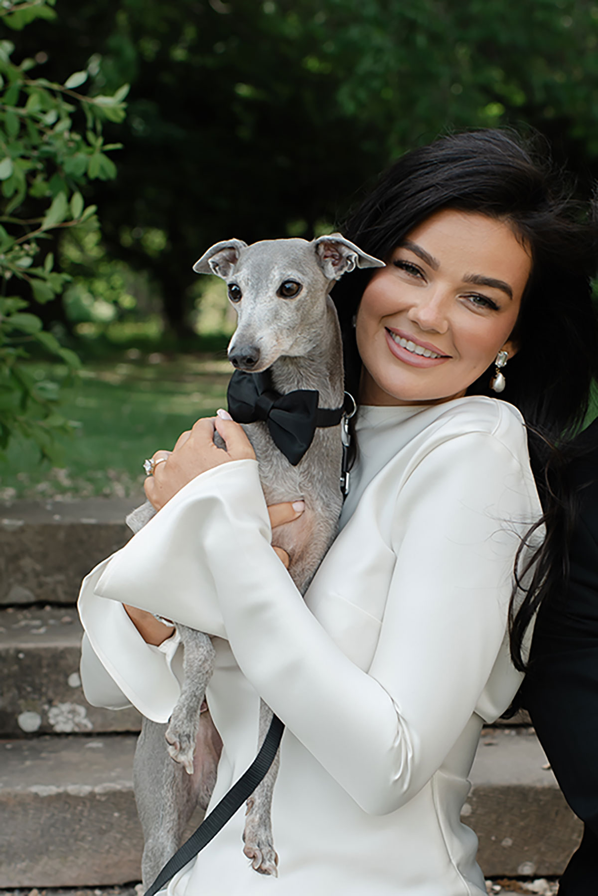 Bride in minimalist long-sleeve wedding dress holding her Italian Greyhound wearing a black bow tie at Carberry Tower
