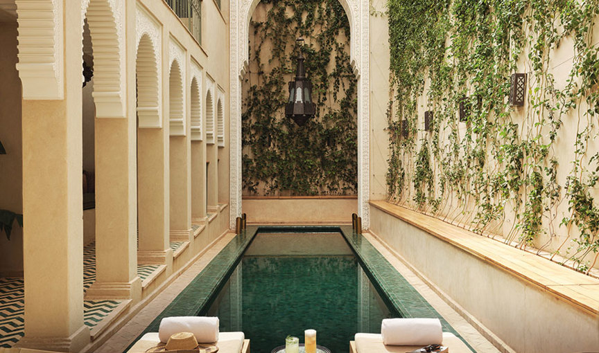 a long narrow pool with chairs and tables in a courtyard with vines growing up walls at Izza Marrakech