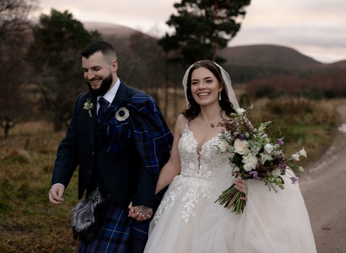 an elated bride and groom walking hand in hand in the countryside. The colours are muted and autumnal