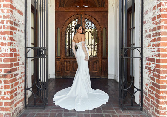 bride looks over her shoulder while stood in front of large wooden door wearing a strapless trailing wedding dress and long tulle gloves