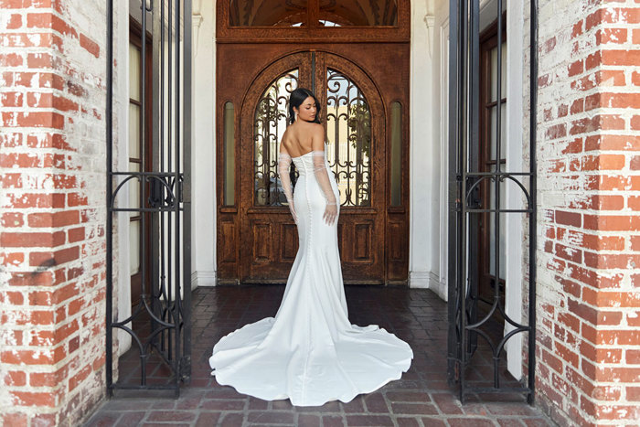 bride looks over her shoulder while stood in front of large wooden door wearing a strapless trailing wedding dress and long tulle gloves