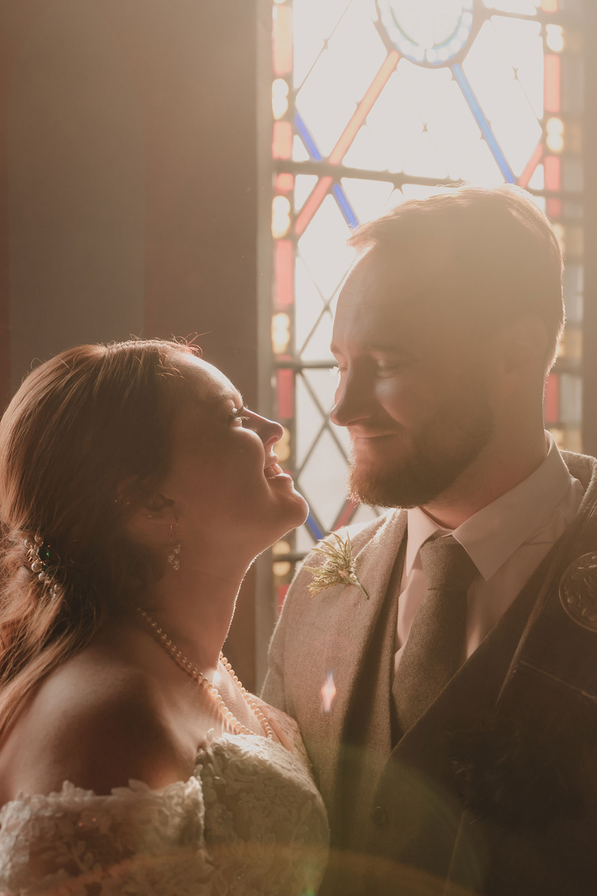 Romantic bride and groom portrait beside stained glass window with warm sunlight at Scottish wedding venue