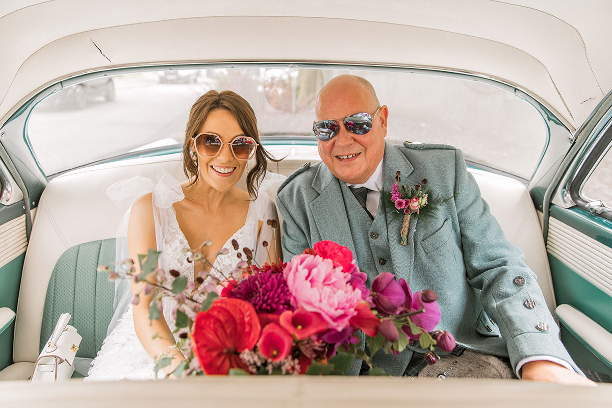 Bride and her father smiling together inside a vintage wedding car