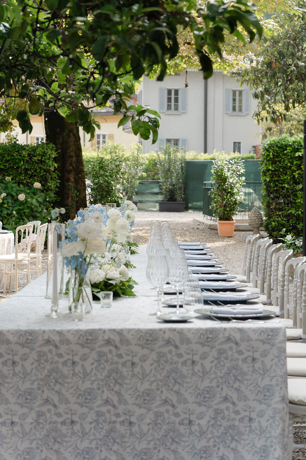 Long outdoor wedding table set for dinner at Villa Regina Teodolinda, featuring white florals, glassware and patterned table linens