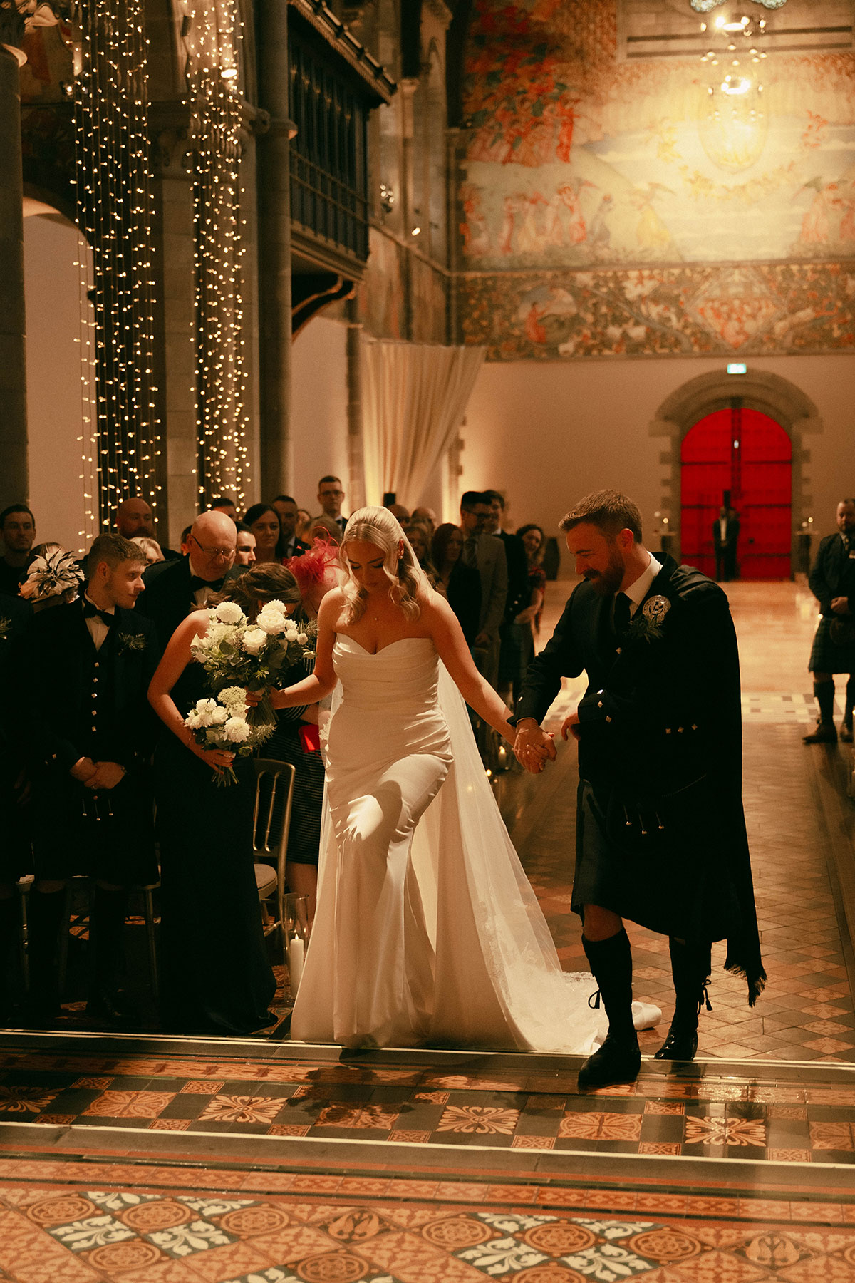 bride and groom walking down aisle together after ceremony with guests and candles