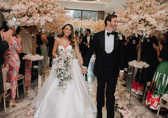 a bride and groom walking up the aisle at Cameron House with cherry blossom trees either side.