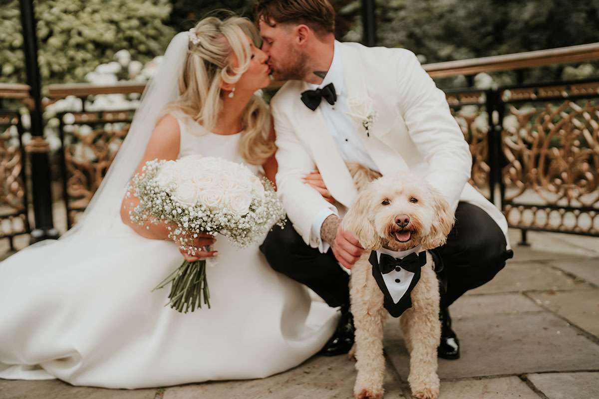 Bride and groom kissing beside dog wearing tuxedo bow tie at Ingliston Country Club wedding