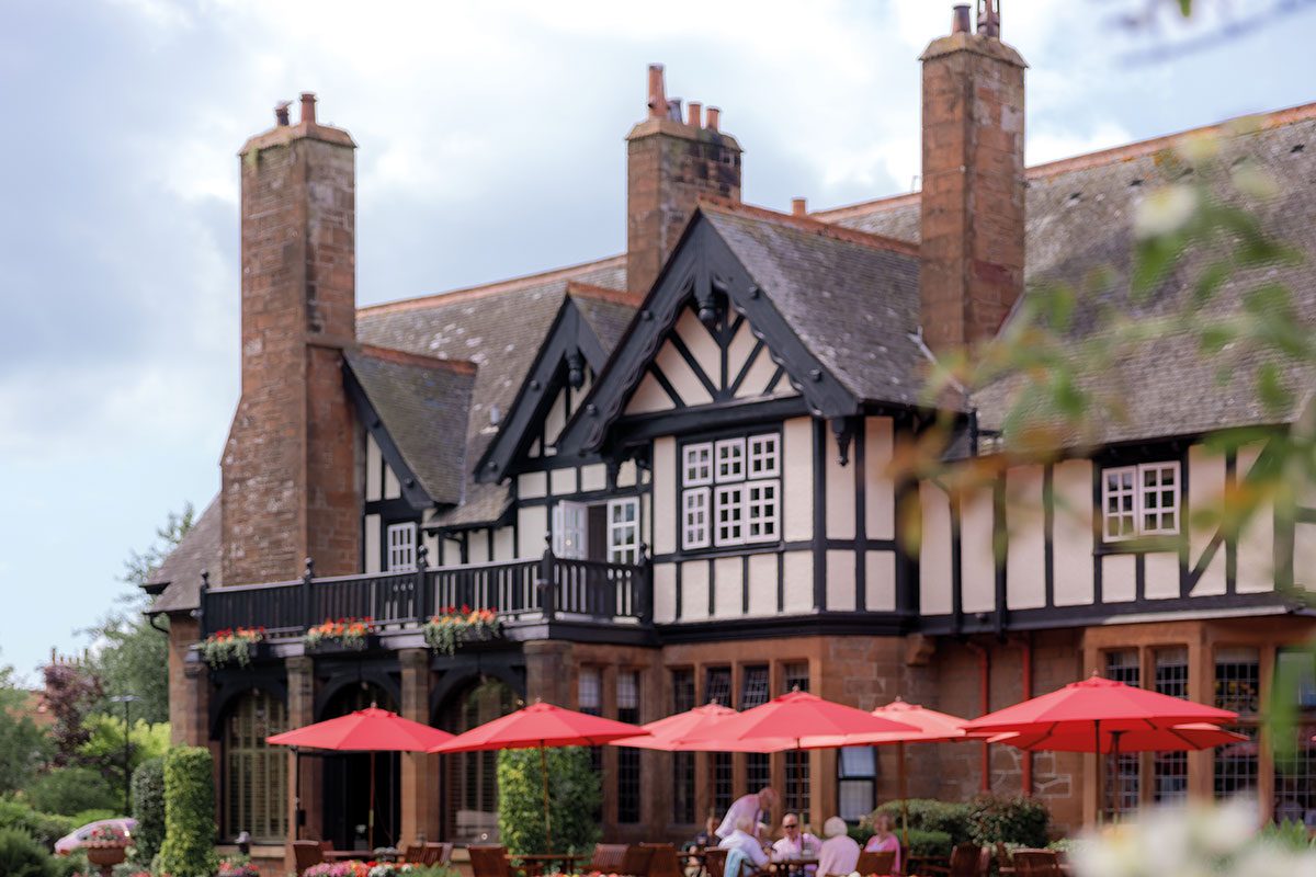 Black-and-white Tudor-style country house with tall chimneys, a balcony and an outdoor terrace with red parasols