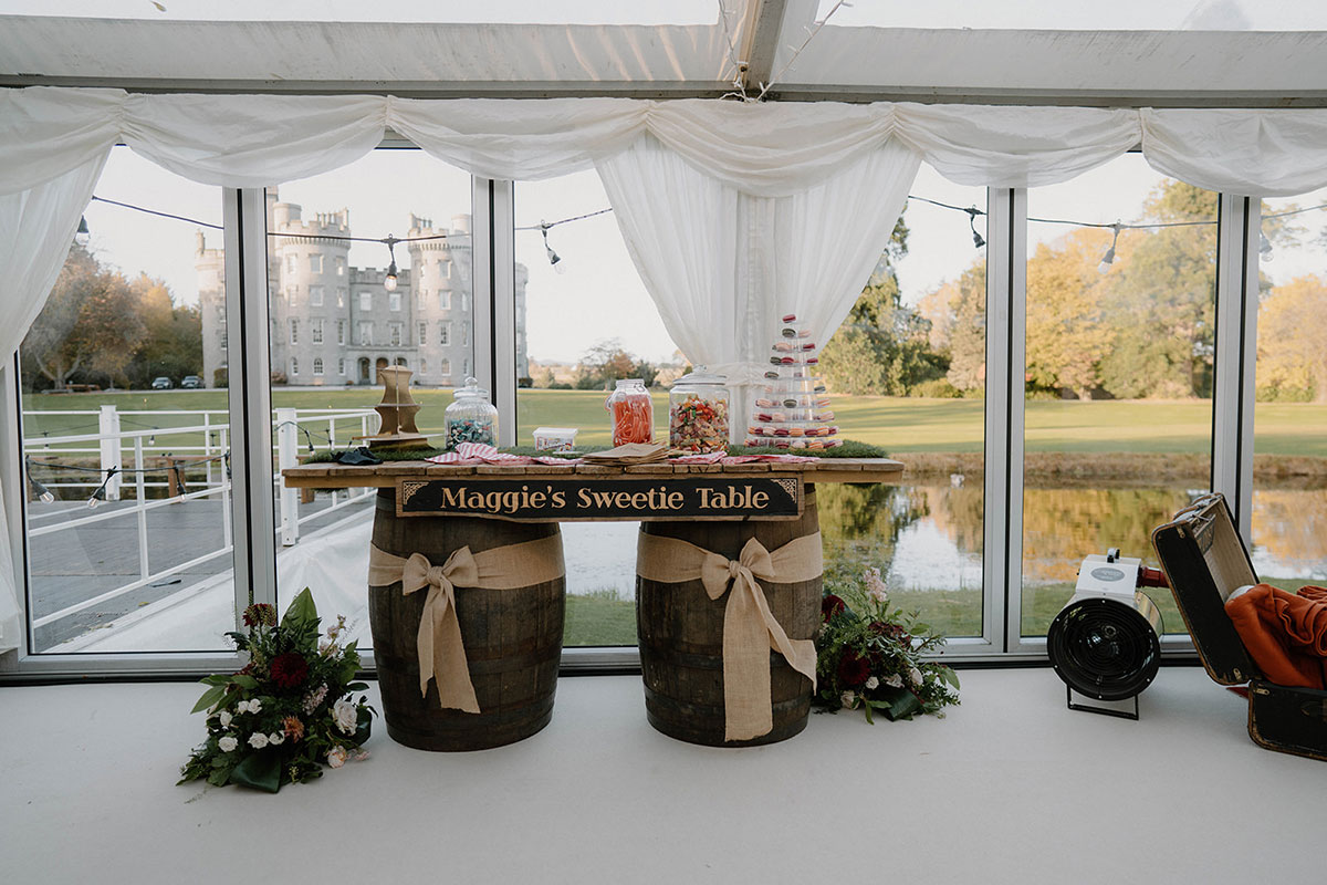 Barrel-style sweetie table with jars and personalised signage inside a wedding marquee at Cluny Castle in Aberdeenshire.