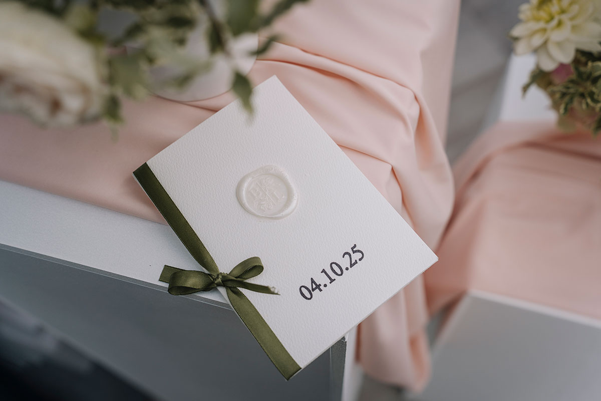 Luxury wedding invitation with wax seal and olive ribbon displaying the date 04.10.25 on soft blush fabric