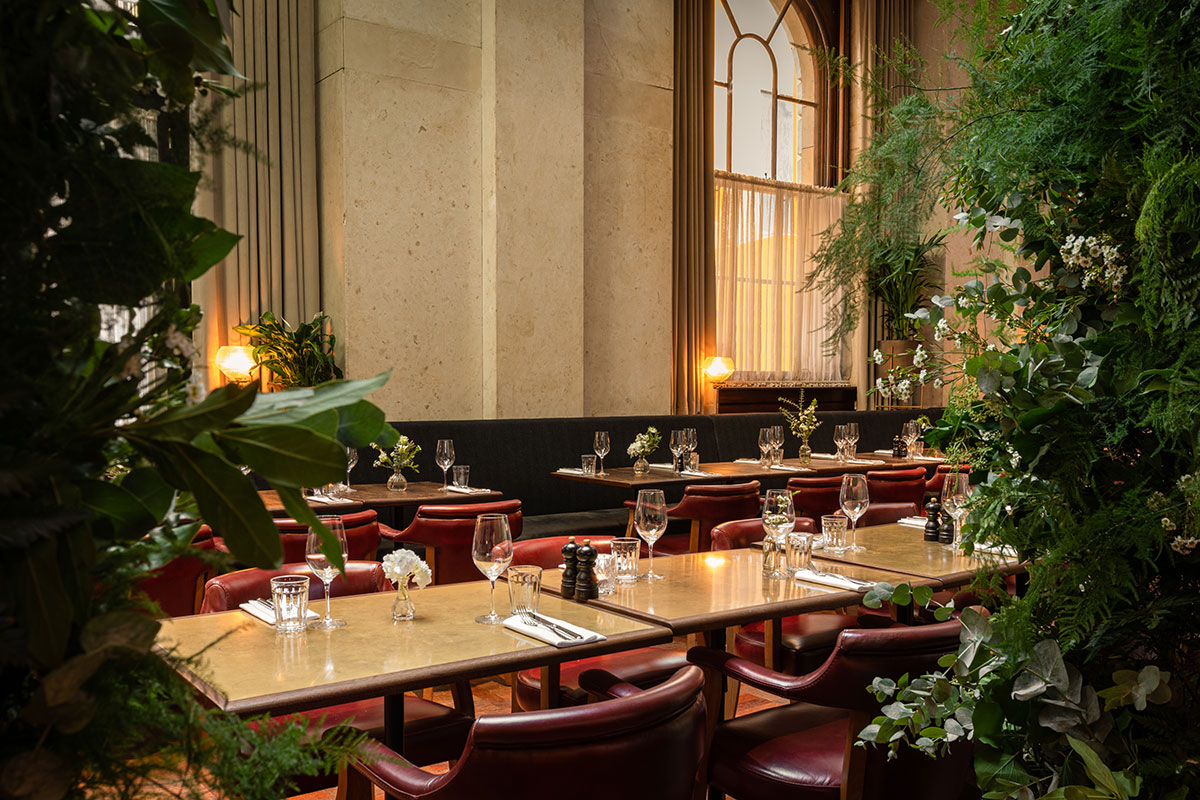 Tellers’ Room at Hawksmoor Edinburgh set for dining with greenery, leather chairs and large arched windows.