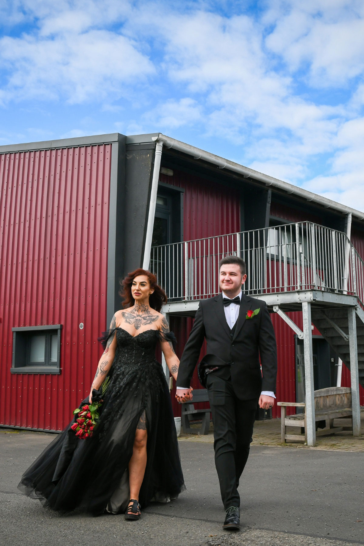 Bride and groom walking hand in hand outside the red and grey barn buildings at Geilsland Estate.