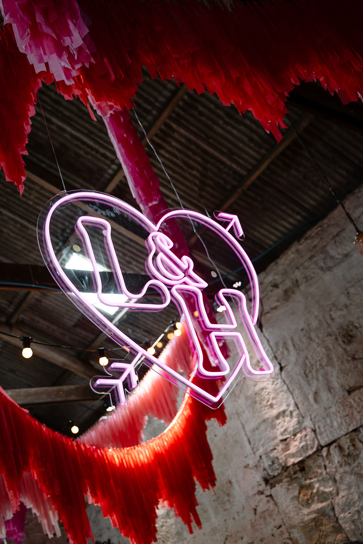 Pink neon sign hanging from ceiling reading 'L&H'