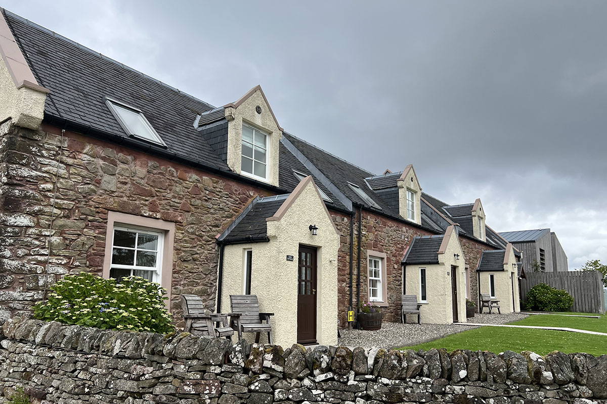 exteriors of three brick cottages attached in a row on a grey sky day