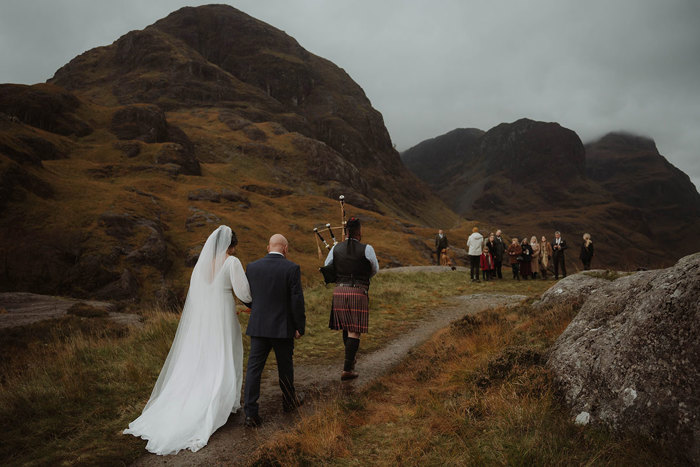 a wedding party and bagpiper walking through Glencoe mountains