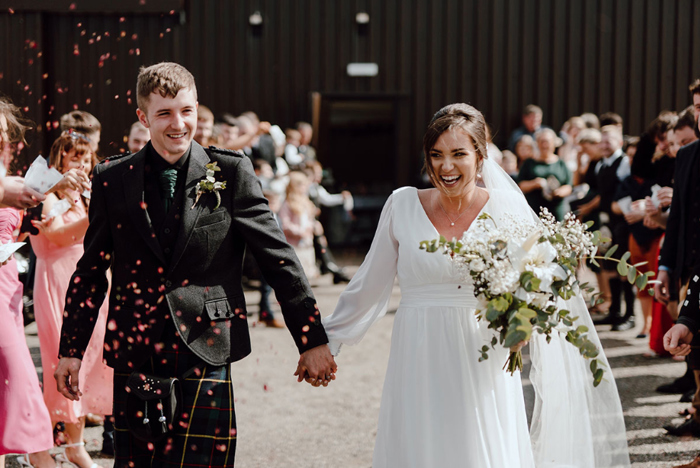 Bride and groom hold hands and look excited as they leave their wedding ceremony