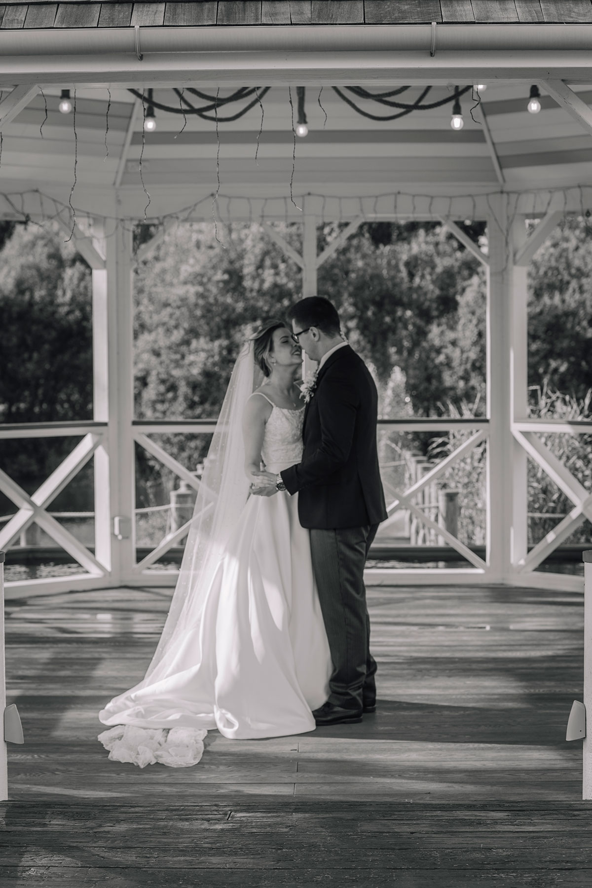 Bride and groom standing together under a white wooden gazebo during outdoor wedding portraits