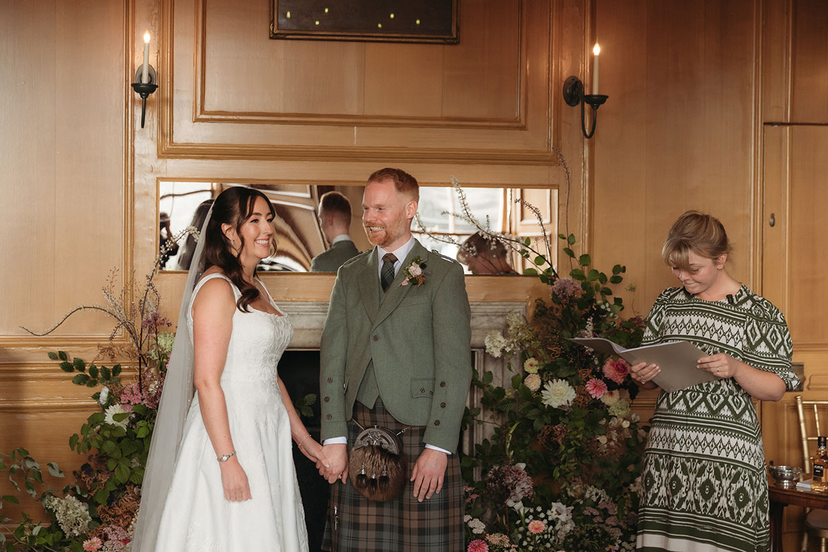 a bride and groom standing during a wedding ceremony in a wood-panelled room at Riddle's Court Edinburgh.