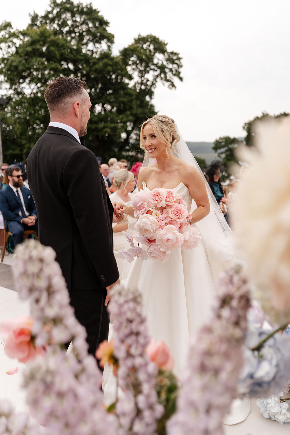 Bride and groom exchange vows during their outdoor Boturich Castle wedding ceremony surrounded by pastel flowers.