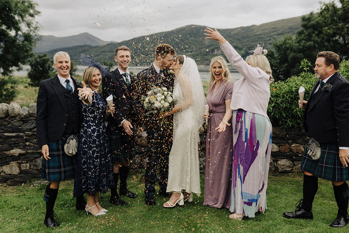 Bride, groom and guests posing amid confetti throw