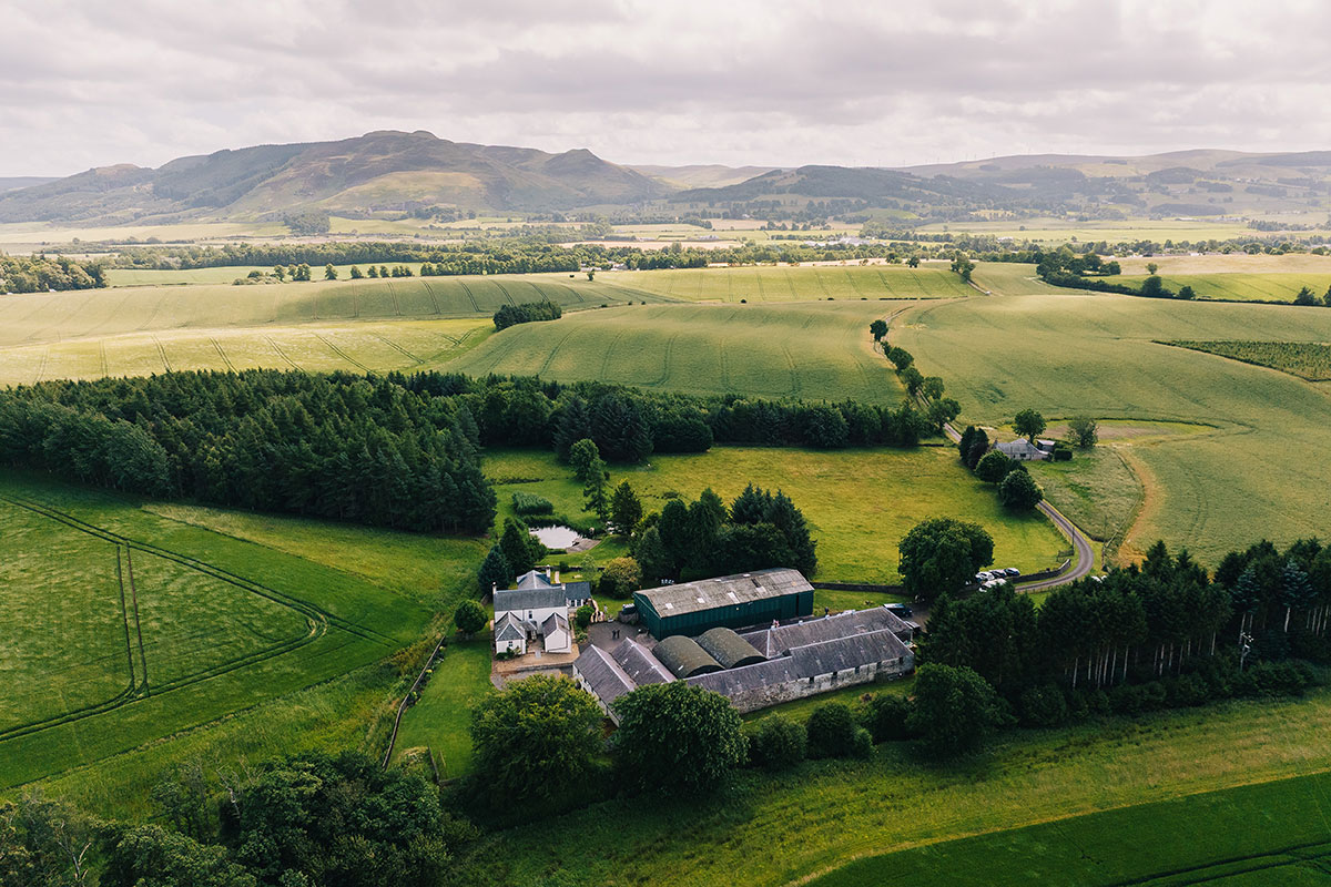 An aerial shot of a farm-style wedding venue surrounded by open fields, woodland and rolling countryside.