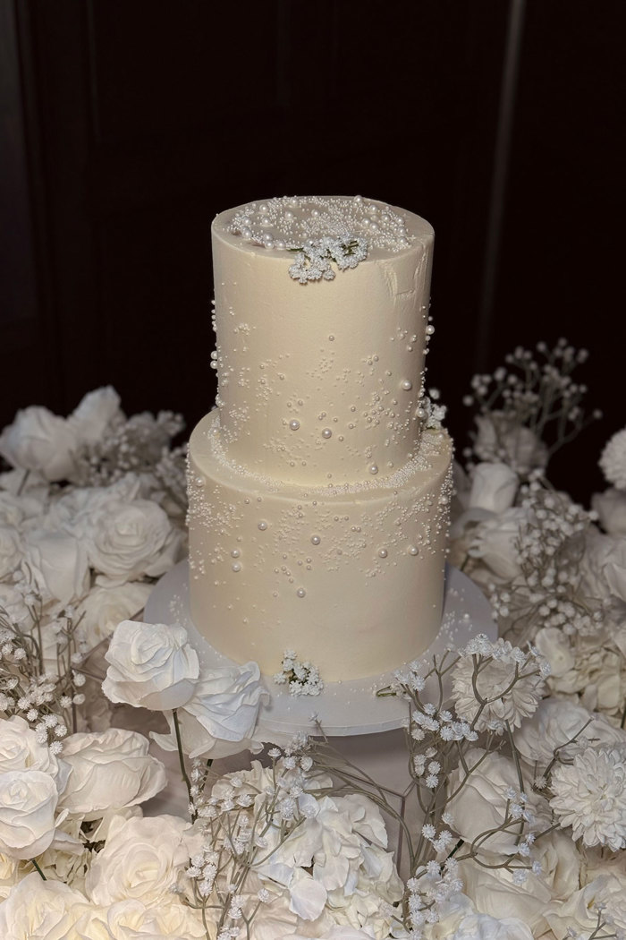 wedding cake with pearl details on a table surrounded by delicate flowers